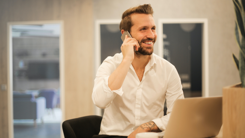 Smiling man on a phone call in front of his laptop